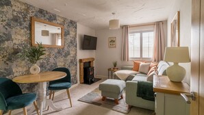 A cozy living room with a fireplace, a dining table with chairs, a sofa, and a television. - Squirrel Bank, with a hot tub & parking (Bowness-on-Windermere)