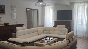 Una sala de estar con un sofá seccional color beige, una mesa de centro, una chimenea y un televisor montado en la pared.