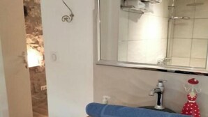 Un baño con un lavamanos de piedra, un espejo y una ducha visible en el reflejo.