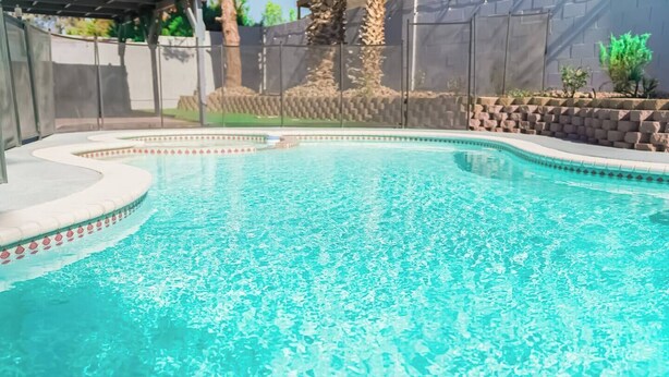 A swimming pool with clear water, surrounded by a stone wall and a fence. - Private house with Pool (Las Vegas)