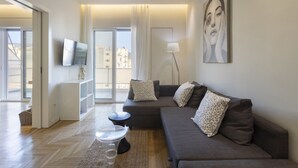 Una sala de estar moderna con un sofá gris, un televisor de pantalla plana, una lámpara de pie y un ventanal con cortinas.
