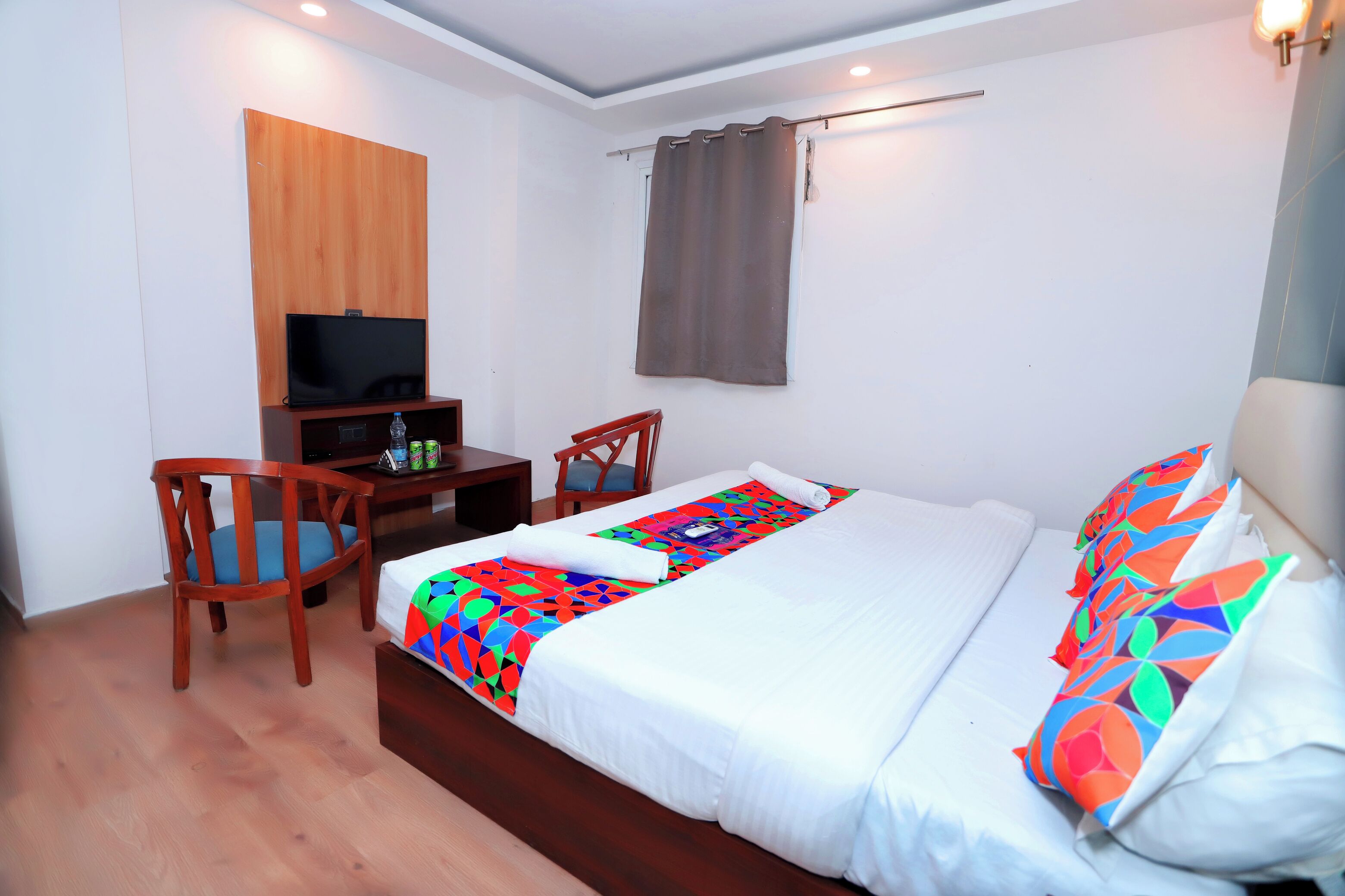 Una habitación de hotel con cama, escritorio, silla, televisor y cortina.