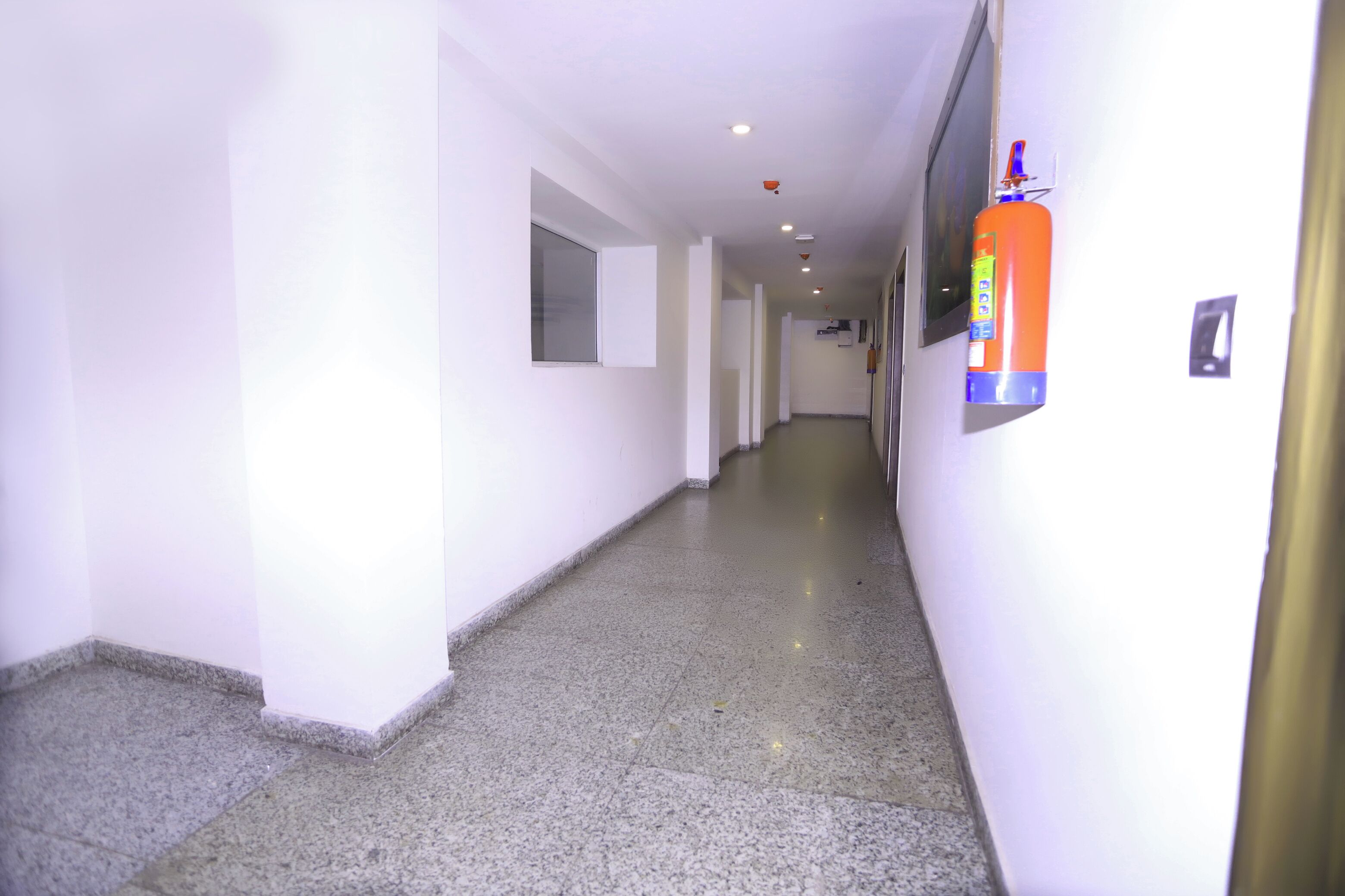 A hallway with white walls, a tiled floor, and a fire extinguisher mounted on the wall.