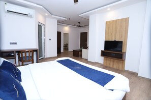 Habitación de hotel con cama, escritorio, silla, televisor y pared de paneles de madera.
