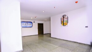 A spacious hallway with a tiled floor, a wooden door, and two framed artworks on the walls. - Hotel Core One Bliss  (Noida)