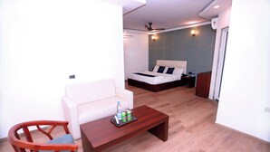 A hotel room with a bed, a white sofa, a wooden coffee table with drinks, and a wooden chair. - Hotel Core One Bliss  (Noida)