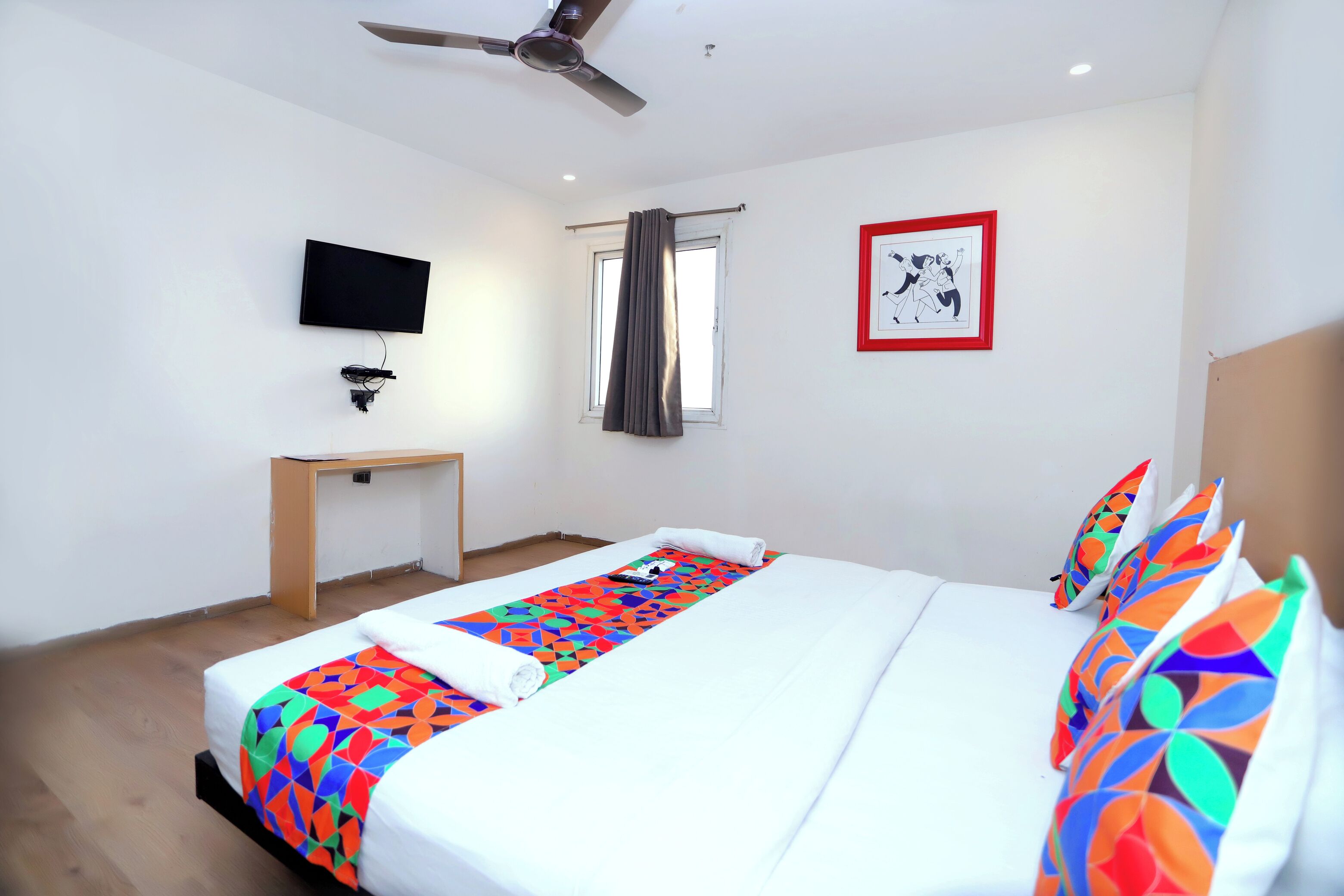 Una habitación de hotel con cama, televisión, escritorio y ventana con cortinas.