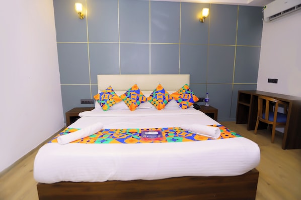 Una cama bien hecha con una colcha colorida y almohadas decorativas, una mesita de noche con una botella y una pequeña mesita auxiliar de madera.
