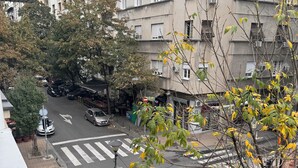 Vista de la calle con un paso de peatones, coches aparcados y un edificio de varios pisos con balcones.