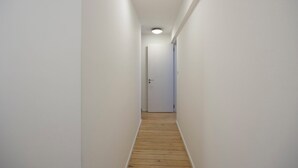Un couloir étroit aux murs blancs, doté d’un plancher en bois et d’une porte au bout.