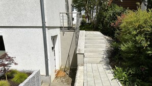 A set of outdoor stone steps leading up to a building entrance, surrounded by greenery and a metal handrail. - Rottweiler Ferienwohnung - Moderne Ferienwohnung mit Nähe zum Wasserturm (Rottweil)
