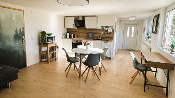 A modern kitchen with wooden cabinets, a dining table with chairs, and a large window. - Rottweiler Ferienwohnung - Moderne Ferienwohnung mit Nähe zum Wasserturm (Rottweil)