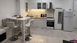 Une cuisine moderne avec des meubles blancs, un coin repas doté d’une table et de chaises blanches, et un réfrigérateur compact.