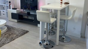 Un salon moderne avec un téléviseur, des meubles blancs, un tableau et une bibliothèque.