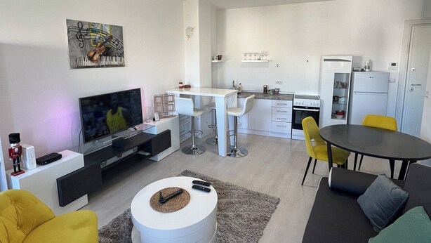 Un salon moderne avec un téléviseur, un fauteuil jaune et une table basse ronde.