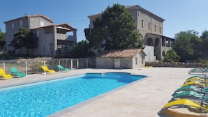 A swimming pool with lounge chairs, a stone building with arches, and a clear sky.