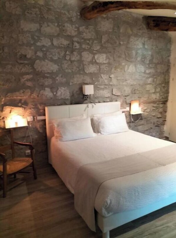 A bedroom with a stone wall, a wooden bed frame, and two bedside lamps. - Virginie's Room (Saint-Alban-Auriolles)