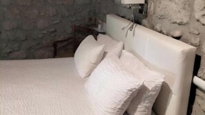 A bedroom with a stone wall, a white bed with multiple pillows, and a bedside table with a lamp.