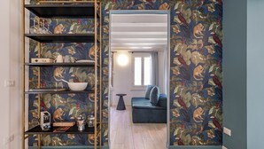 A room with a blue wall, a wooden floor, a blue sofa, and a bookshelf with various items. - The Green Jungle by Wonderful Italy (Venecia)