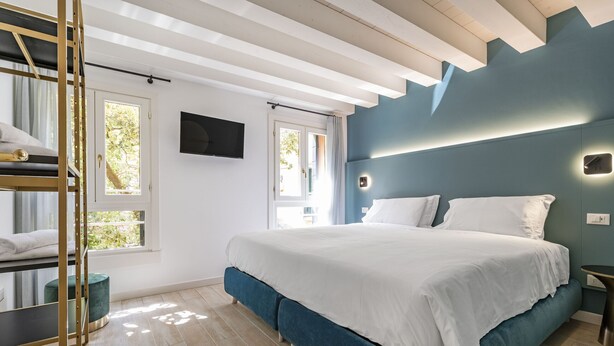 A modern bedroom with a large bed, a bunk bed, a TV, and a window with a view of greenery. - The Green Jungle by Wonderful Italy (Venecia)