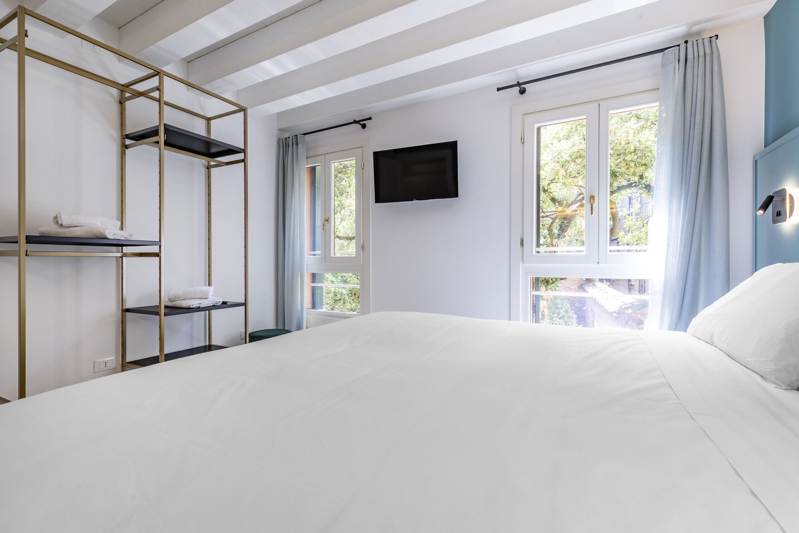 A bedroom with a bed, a TV mounted on the wall, and a window with curtains.