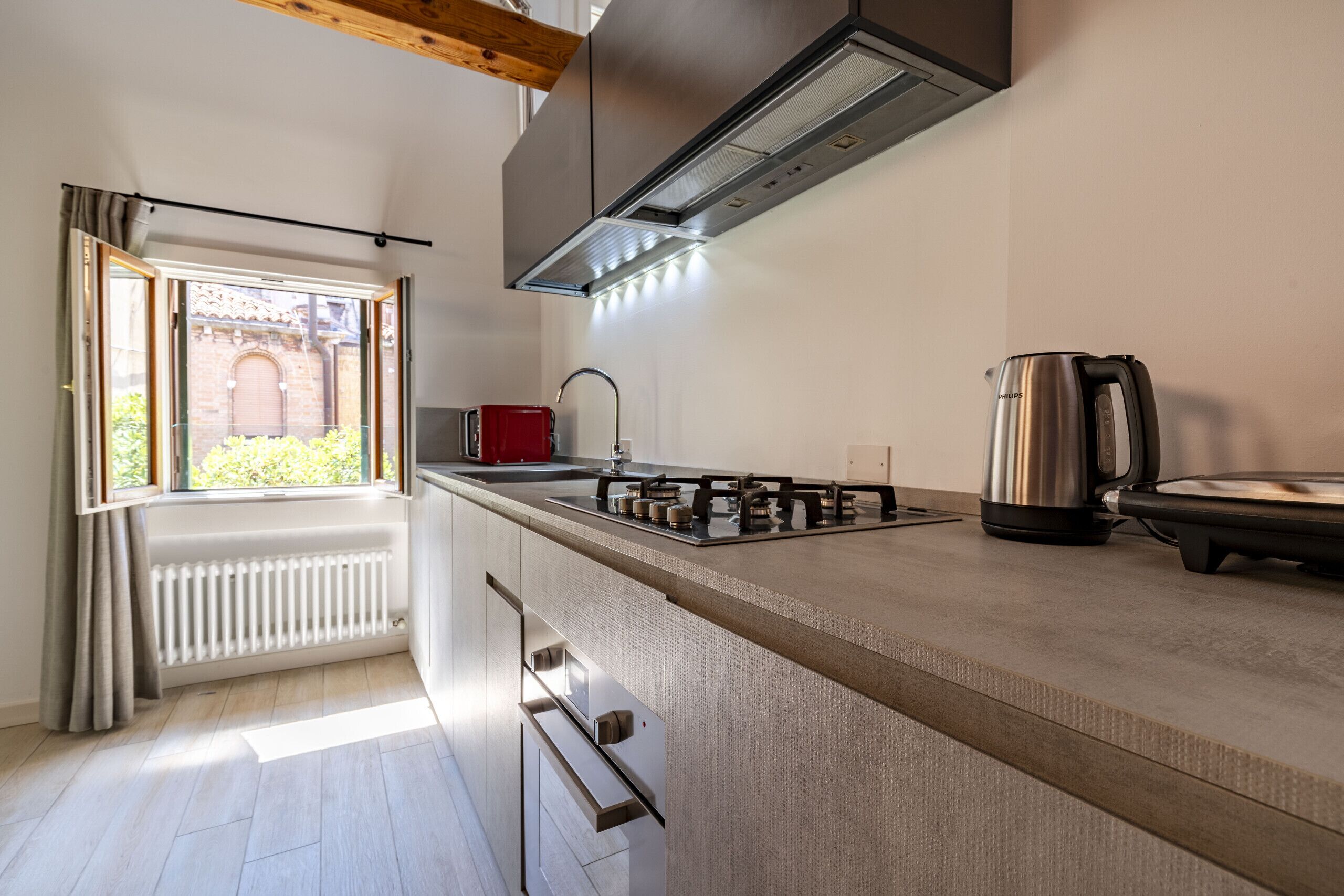 Una cocina moderna con estufa a gas, hervidor y ventana con cortinas.