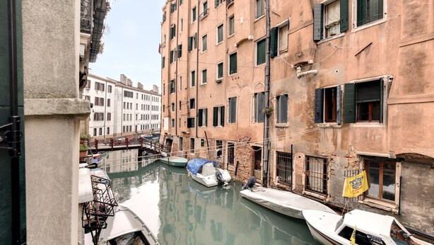 A narrow canal with boats docked along the sides, surrounded by multi-story buildings with balconies and windows. - Marco Polo Apartment by Wonderful Italy (Venecia)