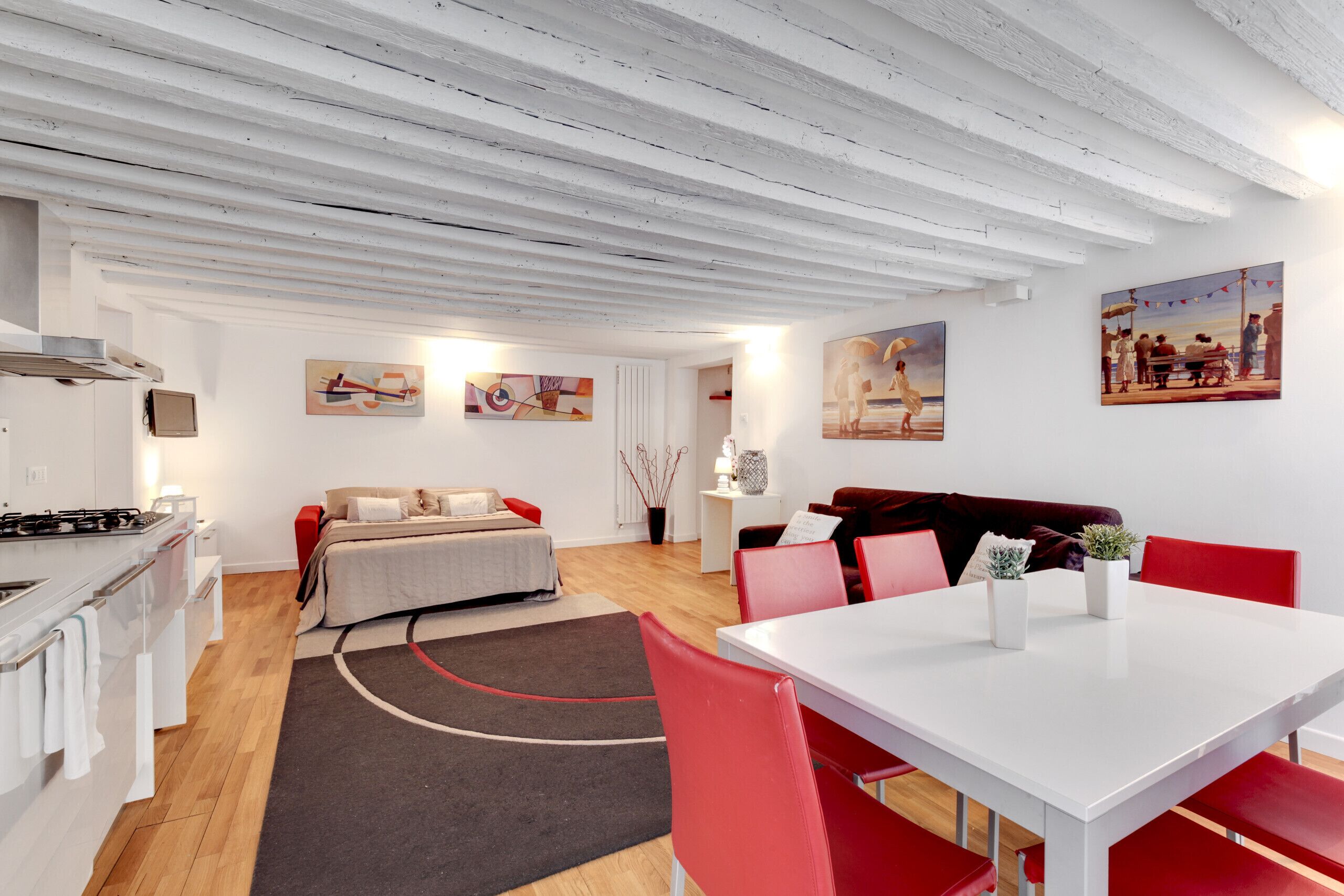 Et moderne, veloplyst rum med en seng, et spisebord med røde stole, et tekøkken og billeder på væggene.