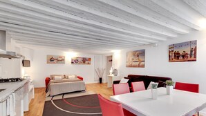 A modern, well-lit room with a bed, a dining table with red chairs, a kitchen area, and artwork on the walls. - Marco Polo Apartment by Wonderful Italy (Venecia)
