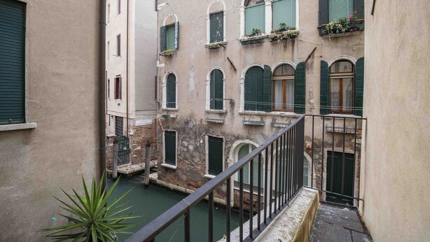 Un canal étroit, bordé de bâtiments de chaque côté, avec des fenêtres en arc et des balcons ornés de plantes.