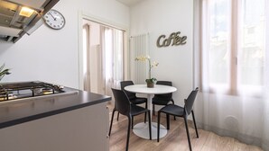 Une cuisine moderne équipée d’une cuisinière, d’une table à manger avec quatre chaises, d’une horloge et d’une enseigne murale sur laquelle on peut lire le mot « Café ».