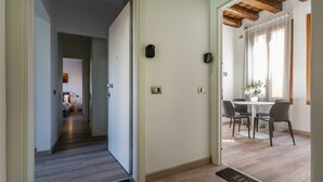 Un couloir mène à une salle à manger dotée d’un plafond en bois, une porte avec une poignée et un paillasson sur lequel est écrit le mot « MAISON ».