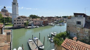 A canal with boats docked, historic buildings, and a prominent tower. - Skyline Penthouse by Wonderful Italy (Venecia)