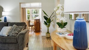 A living room with a grey sofa, a wooden coffee table, and a blue vase. There is a dining area in the background with a table and chairs. - The Canopy on 10th | Game Room • Pets • Pergola (Gainesville)