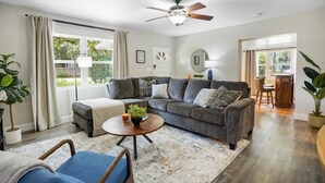 A living room with a grey sectional sofa, a round coffee table, and a ceiling fan. - The Canopy on 10th | Game Room • Pets • Pergola (Gainesville)