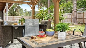 An outdoor patio with a wooden pergola, wicker furniture, a grill, and a table set with a fruit tart and bowls of fruit. - The Canopy on 10th | Game Room • Pets • Pergola (Gainesville)