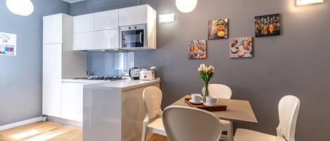 A modern kitchen with white cabinets, a built-in oven, and a dining area with a table and chairs.
