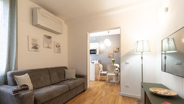 A modern living room with a grey sofa, a dining area with a white table and chairs, and a kitchen visible through an open doorway. - Ca' dei Botteri 4 by Wonderful Italy (Venecia)