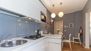 A modern kitchen with a gas stove, stainless steel sink, and white cabinetry. There is a dining area with a table and chairs, and a hallway leading to another room. - Ca' dei Botteri 4 by Wonderful Italy (Venecia)