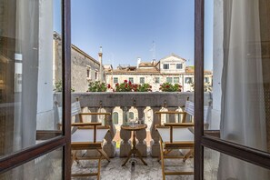 A balcony with two wooden chairs and a small table, overlooking a historic building with a tiled roof and arched windows.