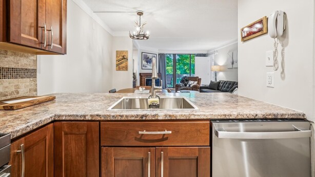A kitchen with wooden cabinets, a granite countertop, a stainless steel sink, and a dishwasher.