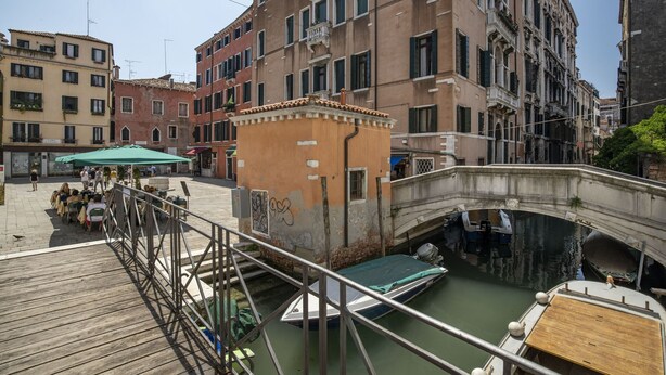 Un canal où naviguent des bateaux, un pont en bois et des bâtiments dotés de balcons.