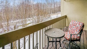 A balcony with a view of leafless trees and a snow-covered ground, a small round table, and a single patterned chair. - Pinnacle F06 Condo | Pool, Hot Tub | Golf Nearby (Killington)