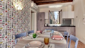 A dining area with a round table set for four, surrounded by blue chairs. The walls feature a patterned wallpaper, and there is a view of a street through a window. - Rugabella Rialto by Wonderful Italy (Venecia)