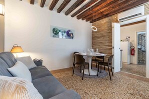 A modern living room with a grey sofa, a dining table with chairs, a painting on the wall, and a wooden ceiling. - Rialto Ca’ del Mercante by Wonderful Italy (Venecia)