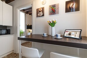 Eine moderne Küche mit dunkler Arbeitsplatte, weißen Stühlen, einer weißen Vase mit Tulpen und einem Tablet, das eine Webseite anzeigt.