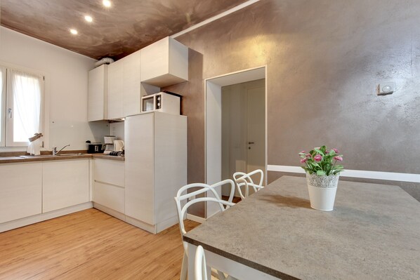 A modern kitchen with white cabinets, a built-in microwave, and a dining area with a table and chairs. - San Marco Promenade by Wonderful Italy (Venecia)