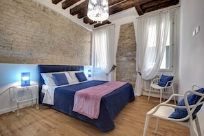 A bedroom with a large bed, a nightstand, a chair, and a window with curtains. - San Marco Promenade by Wonderful Italy (Venecia)