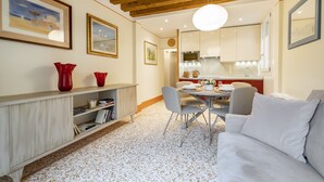 Una sala de estar moderna con un sofá blanco, una mesa de comedor con sillas, una zona de cocina con armarios y un techo de madera.