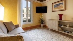 Una sala de estar con un sofá, un televisor montado en la pared, una planta en maceta y una estantería.